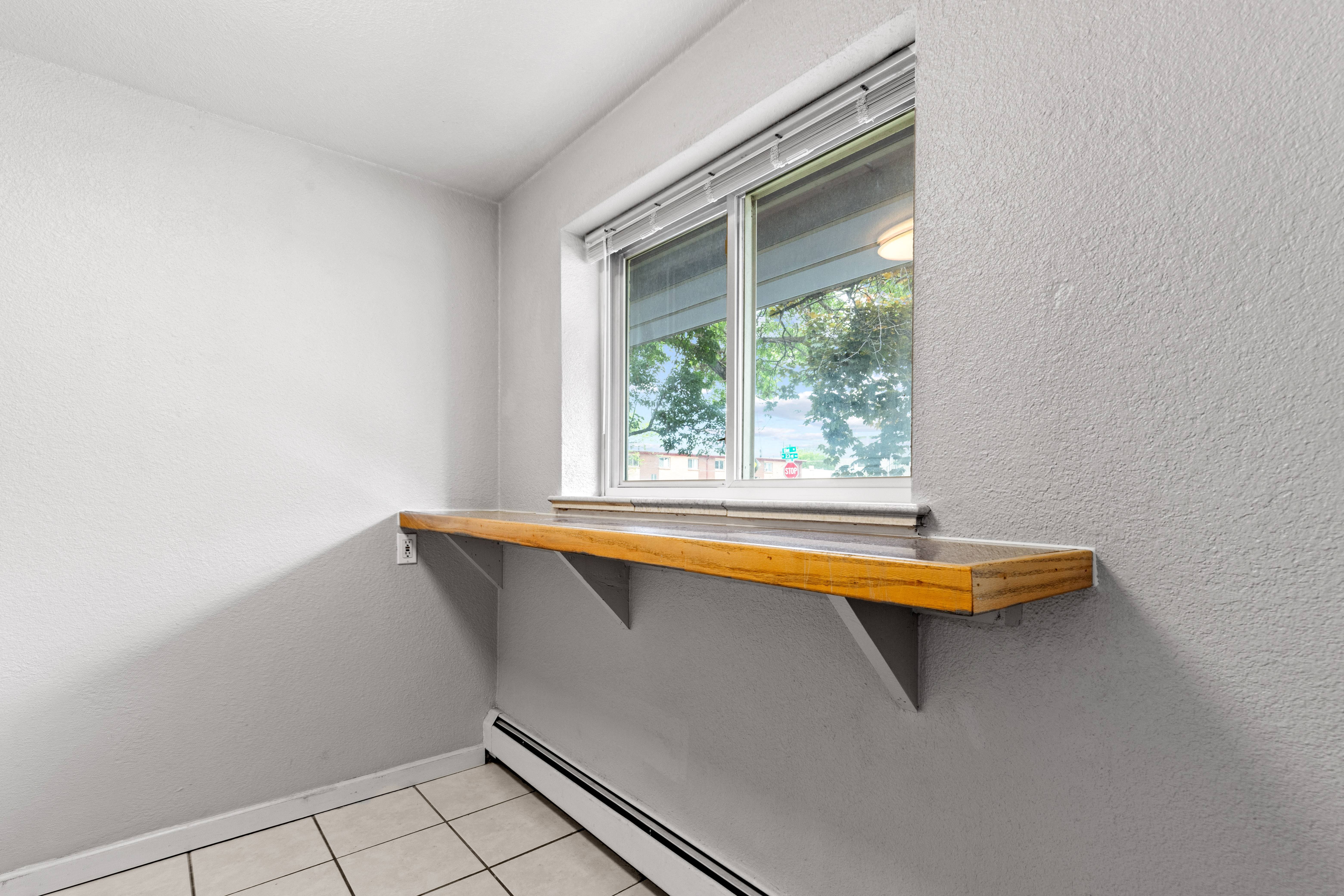 a window with a wooden sill in a white room with a tiled floor